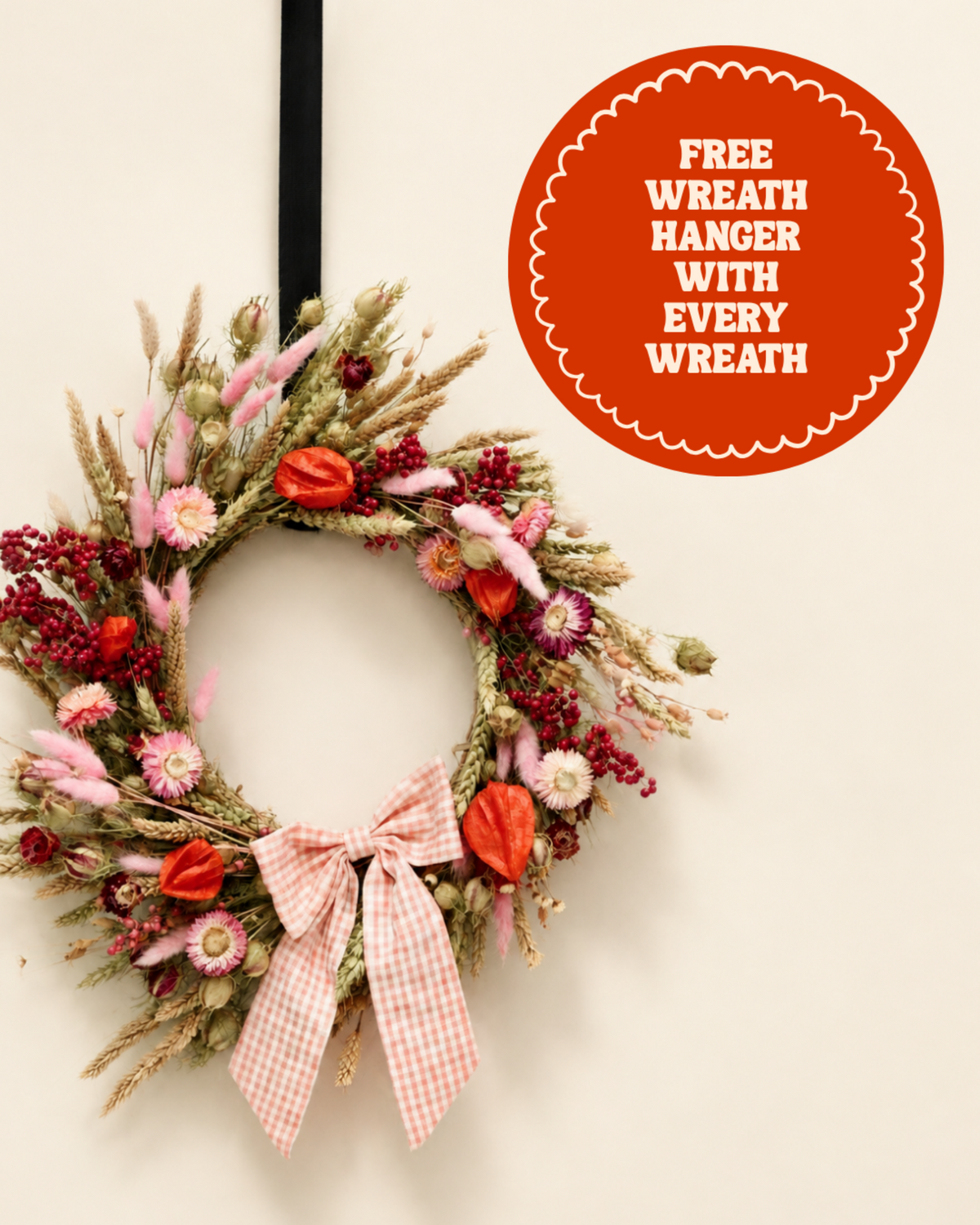 The Crate dried floral door wreath with pink strawflowers, natural grain stems, and a pink gingham ribbon. Premium long-lasting dried flower decor, comes with a free black over-door hanger badge.