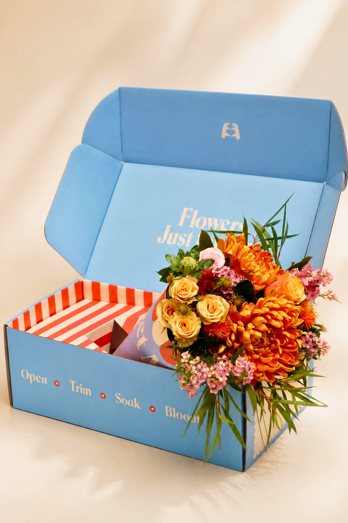 Forget Me Not bouquet delivery in a blue gift box by The Crate, featuring orange chrysanthemums, peach roses, and pink waxflowers. Direct-to-door fresh flower delivery with "Open, Trim, Soak, Bloom" care steps printed on the box.