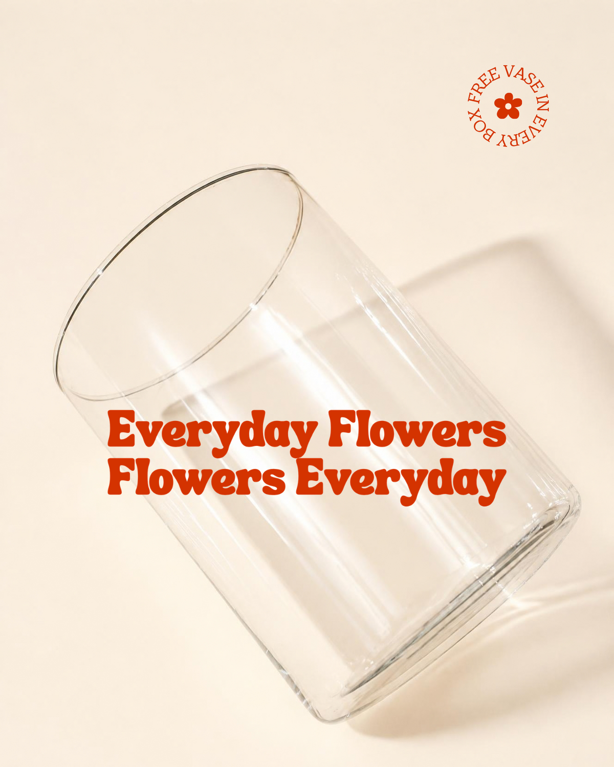 A clear cylindrical glass candle vessel shown on a warm cream background with orange text reading 'Everyday Flowers Flowers Everyday' across the front and a small circular red logo in the top right.