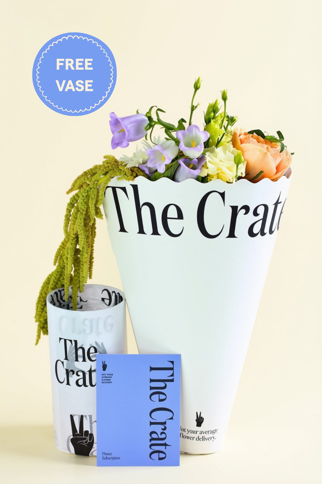 A floral arrangement in a white conical cone printed with 'The Crate,' shown with two matching branded vases and a blue card on a light cream background. A circular badge reads 'FREE VASE.